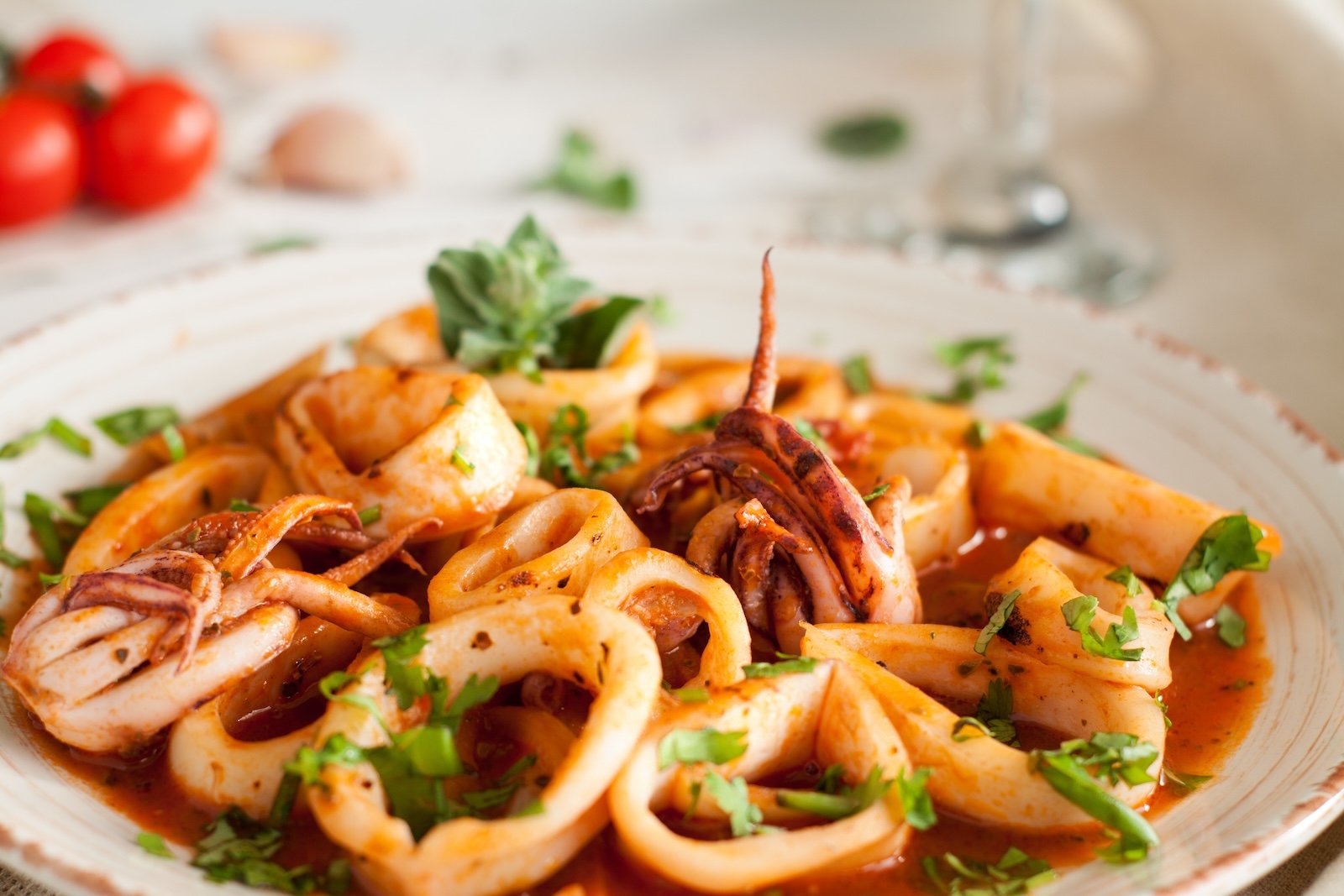 Salad with calamari, octopus, parsley and tomato sauce on light wooden table