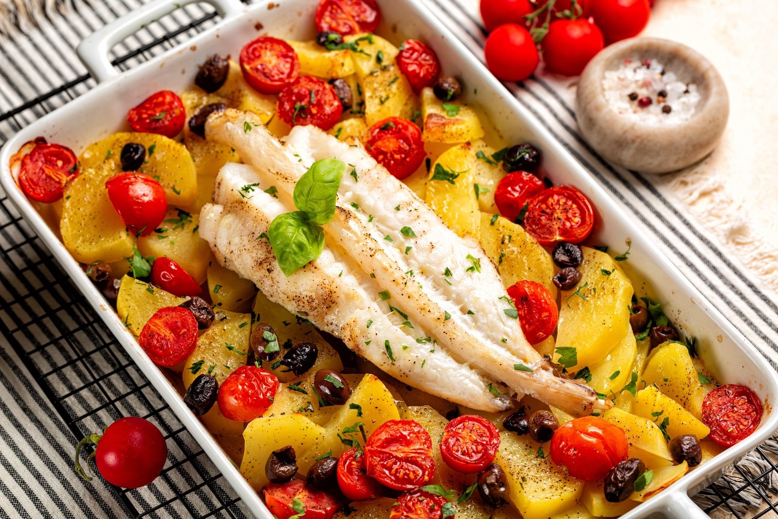 Oven baked anglerfish, monkfish with potato, olives, parsley and tomatoes. Cooked fish dinner in a white casserole. Italian style dinner.